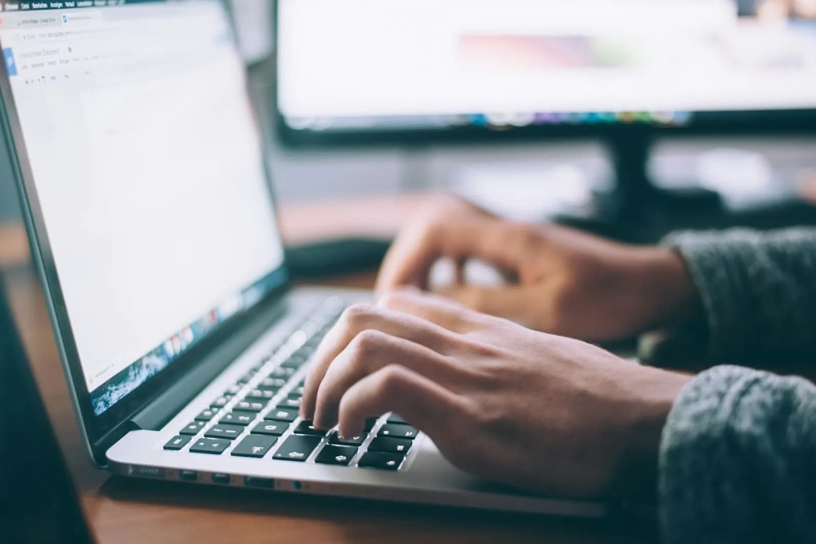 Hände tippen auf der Tastatur eines aufgeklappten Laptops
