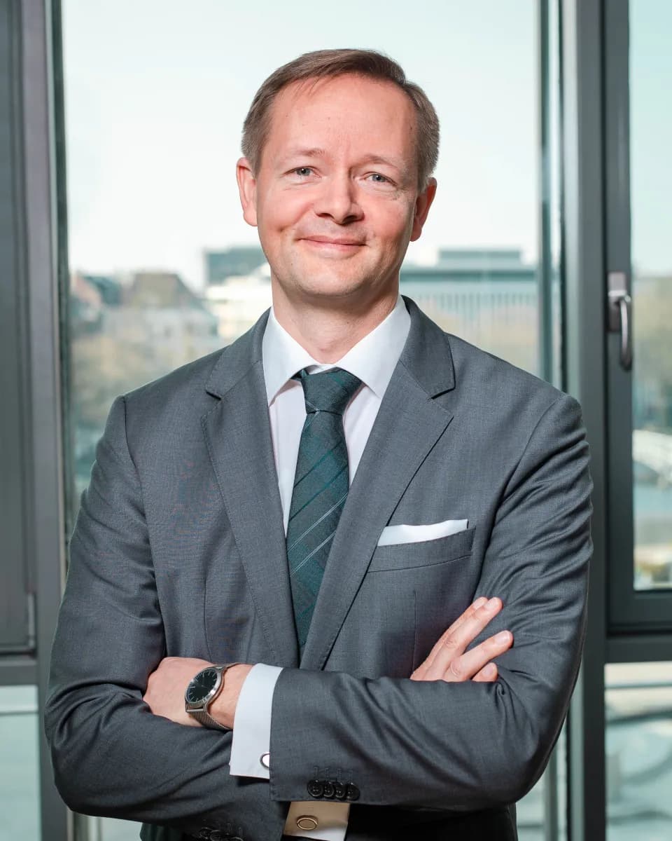 Porträt von Dr. Lars Holldorf im grauen Anzug vor einem Bürofenster